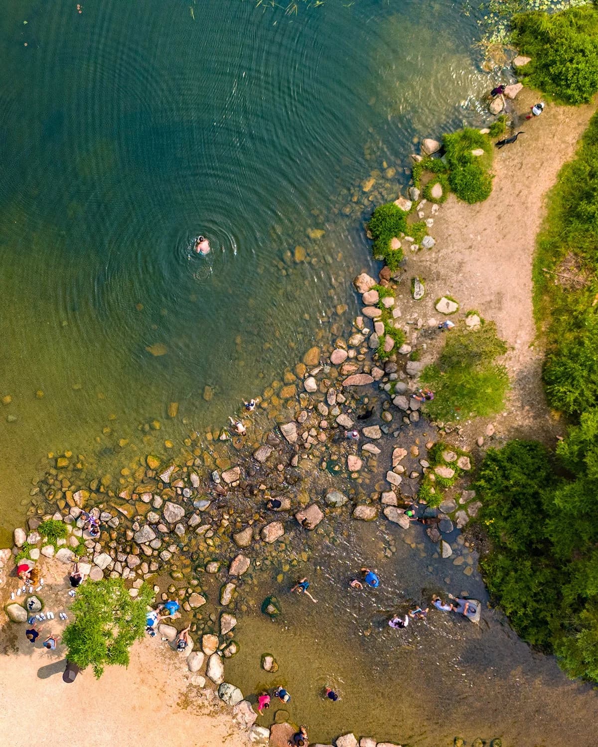 Aerial view of a river with swimmers and rocky shores surrounded by green trees