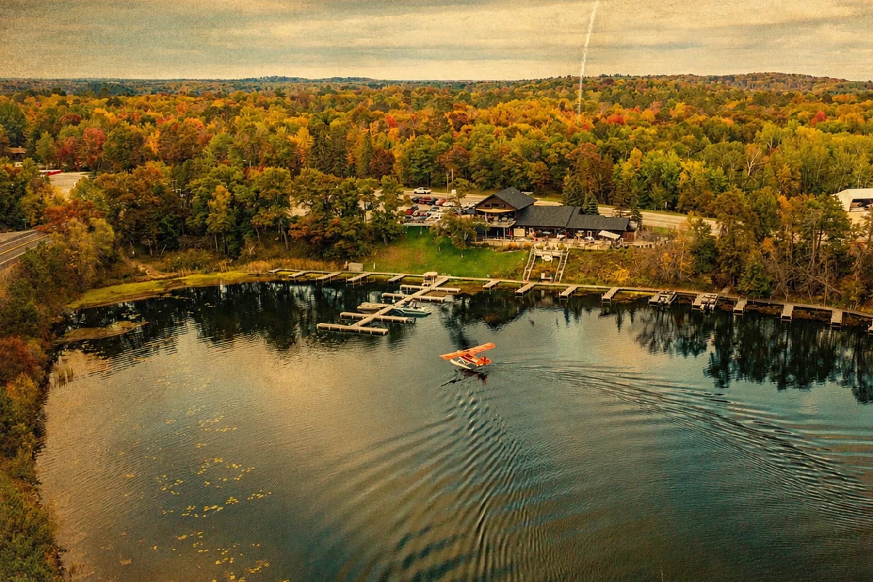 Aerial view of a Minnesota lake with a seaplane taking off, surrounded by autumn-colored trees